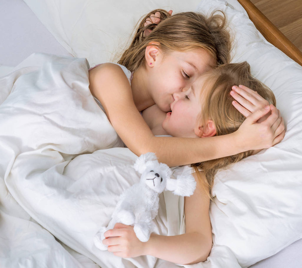 dos hermanas pequeñas abrazándose en la cama
 - Foto, Imagen