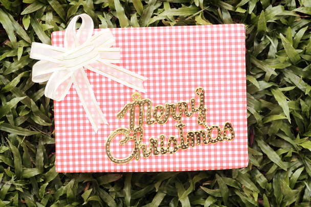 緑の芝生とメリー クリスマスのゴールド テキストにピンクのギフト ボックス. - 写真・画像