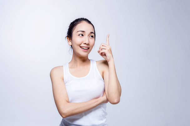 Portrait of a beauty asian smiling girl pointing finger up at copyspace isolated on a gray background - Φωτογραφία, εικόνα