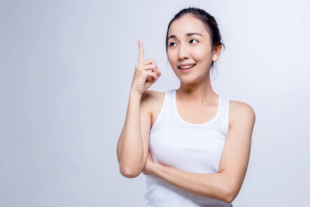 Portrait of a beauty asian smiling girl pointing finger up at copyspace isolated on a gray background - Фото, изображение