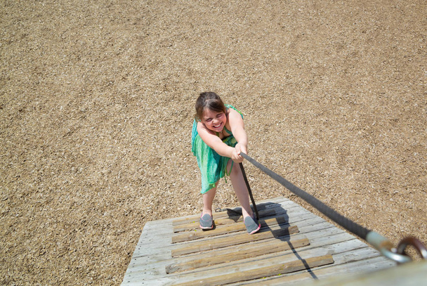  pieni tyttö, jolla on hauska ilme leikkii, kiipeää puisilla portailla ulkona puistossa
 - Valokuva, kuva