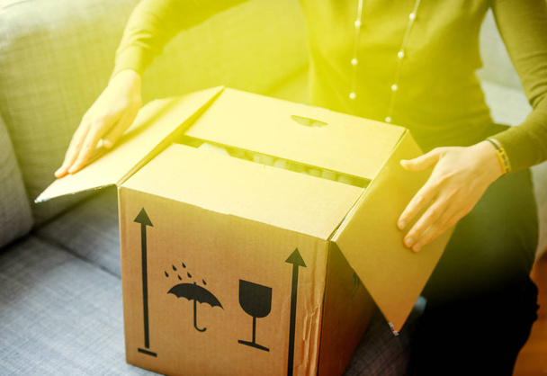 Elegant woman unpacking unboxing cardboard carton box with protective foam pads inside after buying ordering online via internet a present good with green illumination light coming from the box  - 写真・画像
