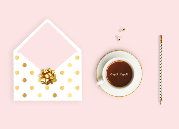 Flat lay. Pink background, envelope pattern polka gold, coffee cup and pencil. Business desktop. - Foto, afbeelding