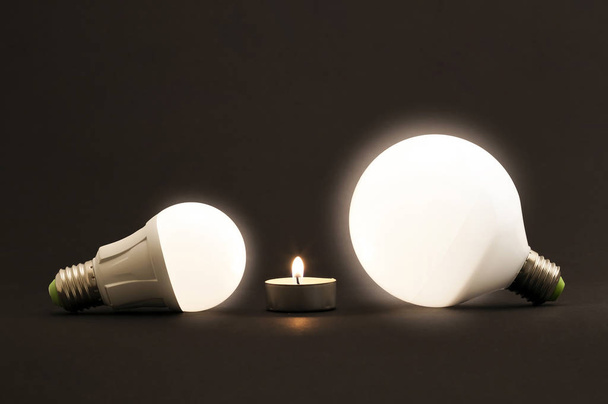 Piccola candela bianca e lampadine elettriche a LED su sfondo scuro. C
 - Foto, immagini