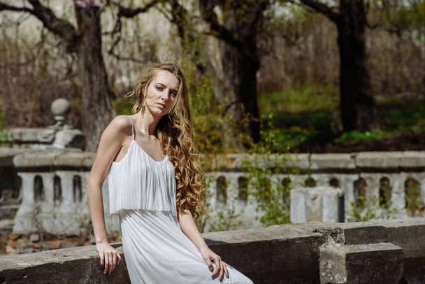 Outdoor summer portrait of young pretty cute girl. Beautiful woman posing at old bridge.  in white dess standing near stone railing. Photo has an  model. - Zdjęcie, obraz
