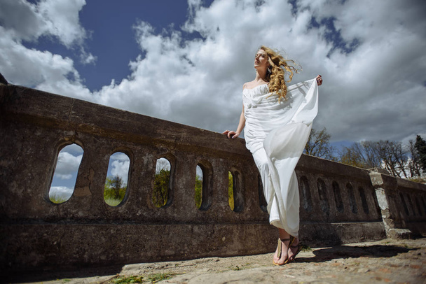 Outdoor summer portrait of young pretty cute girl. Beautiful woman posing at old bridge.  in white dess standing near stone railing. Photo has an  model. - Photo, image