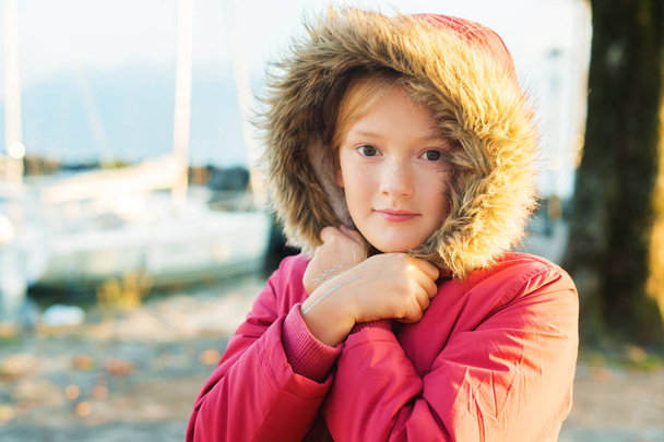 Outdoor close up portrait of cute 9-10 year old little girl wearing warm winter jacket with hood and fur - Photo, Image