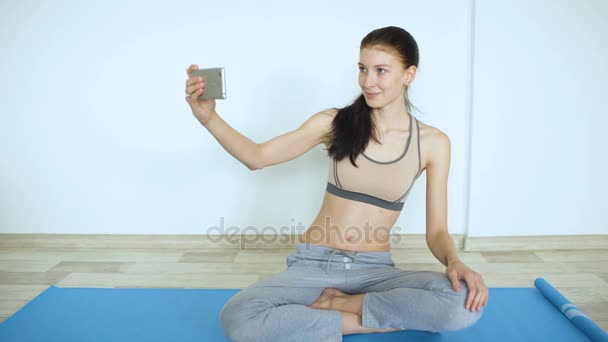 Mujer joven haciendo ejercicio de yoga haciendo sonrisa selfie en smartphone
 - Imágenes, Vídeo