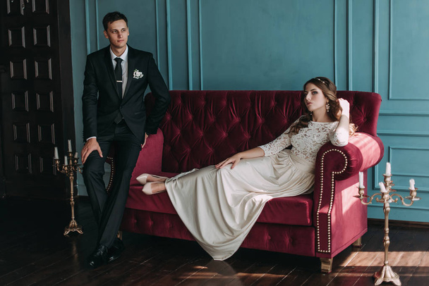 cute wedding couple in the interior of a classic studio posing at the sofa . hey kiss and hug each other, holding hands looking at each other - Foto, Imagen