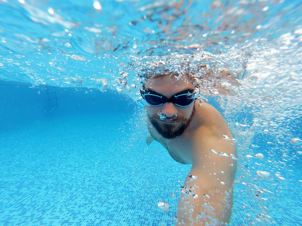 Γενειάδα άνδρας με γυαλιά βουτιές κάτω από το νερό της πισίνας - Φωτογραφία, εικόνα