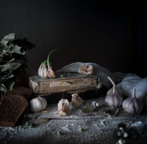 rustic still life, vintage. garlic, rye bread, flour, and old books on a wooden table - Zdjęcie, obraz