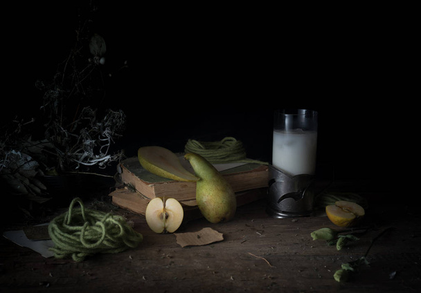 still life, vintage. old books, bouquet of flowers, pear, milk on a wooden table. dark backgrounds - Photo, Image