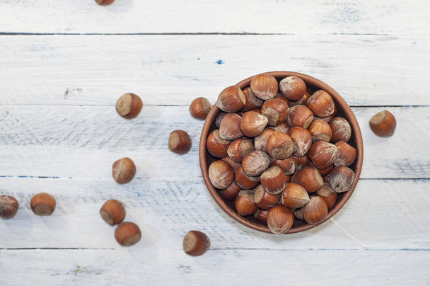 Hazelnuts in shell in brown clay bowl, top view - Zdjęcie, obraz