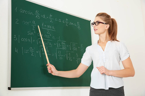 Young teacher with pointer beside blackboard on white background - Фото, изображение
