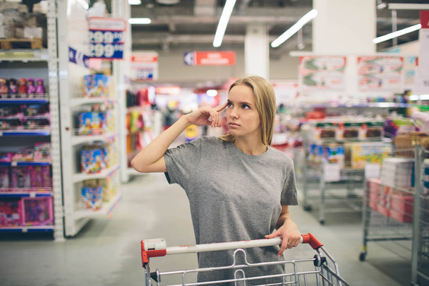 Curious Woman in The Supermarket . Young girl in a market store with  shopping thinking what to buy - Foto, afbeelding