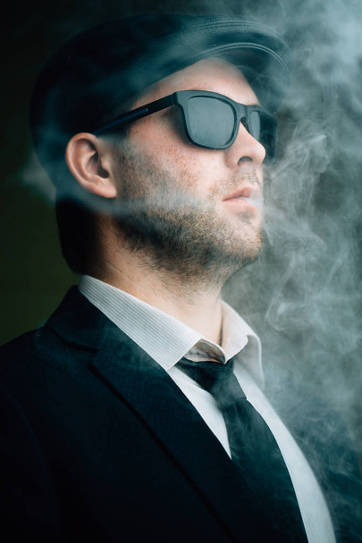 чоловік носить сонцезахисні окуляри і шкіряну шапку в диму
 - Фото, зображення