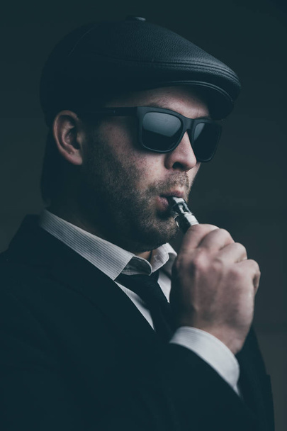 Fashionable man in sunglasses and a leather cap smokes - Fotoğraf, Görsel
