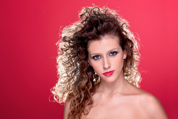 Beautiful woman with curly hair, with light from behind, on red - Fotó, kép