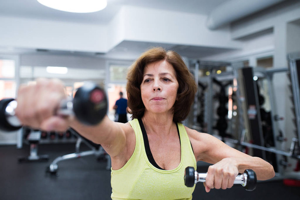 Senior woman in gym working out with weights. - 写真・画像