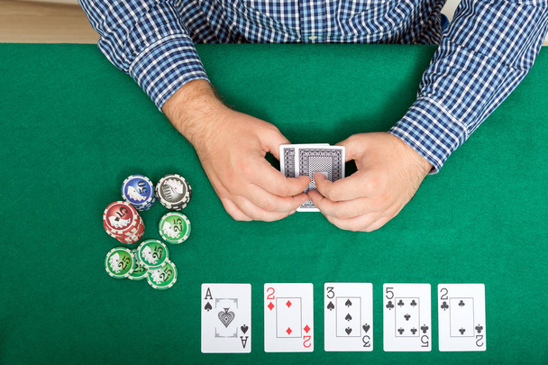 chips and cards for poker in hand on green table, top view - Foto, afbeelding