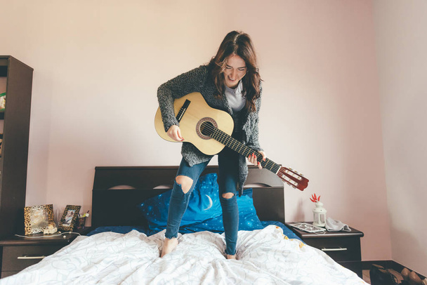 Fiatal gyönyörű keleti nő áll az ágyán gitározik - lány erő, zene, szórakozás koncepció - Fotó, kép