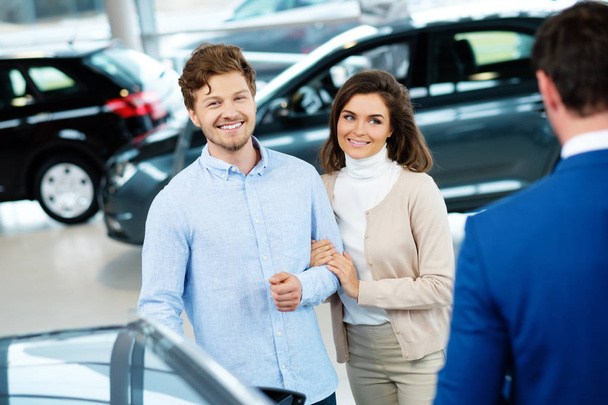 Salesman talking to a young couple at the dealership showroom - Photo, Image