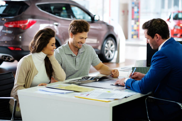 Beautiful young couple reading a booklet at the dealership showroom - Photo, Image