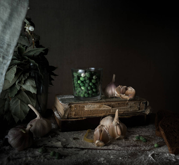 rustic still life, vintage. green peas, old books, garlic, flour on a wooden table. dark background - Foto, afbeelding