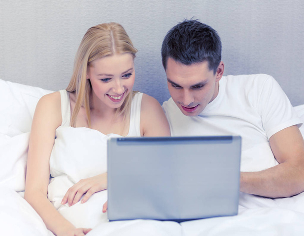 smiling couple in bed with laptop computer - Foto, imagen