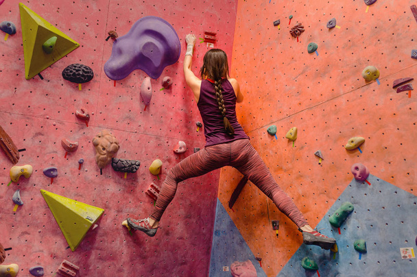 Mujer joven practicando en bouldering en una pared de roca dentro
 - Foto, imagen