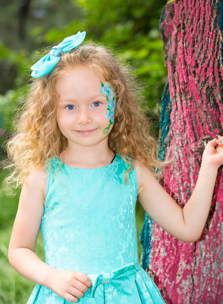 Beautiful happy girl kid with aqua make-up on birthday in park. Celebration concept and childhood, love - Zdjęcie, obraz