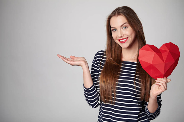 Smiling woman holding red polygonal paper heart shape - Foto, Imagen