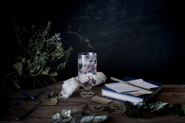 still life, vintage. a glass of mineral water and berries, books, bouquet on  wooden table. dark backgrounds - Fotó, kép