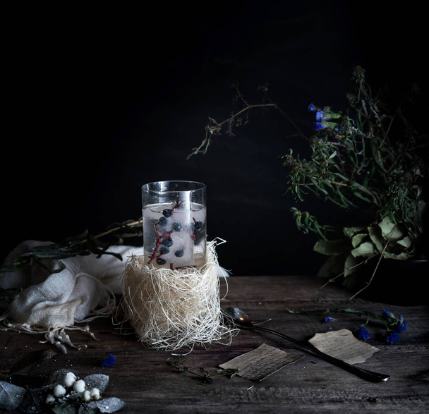 still life, vintage. a glass of mineral water and berries, books, bouquet on  wooden table. dark backgrounds. . - Foto, afbeelding