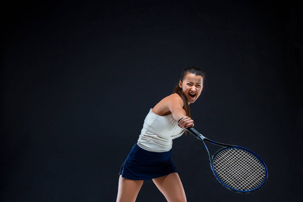 Portrait of beautiful girl tennis player with a racket on dark background - 写真・画像