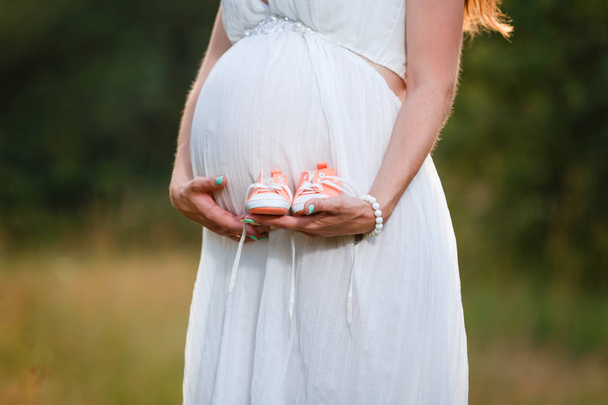 Kleine schoenen voor de ongeboren baby in de buik van een zwangere vrouw - Foto, afbeelding