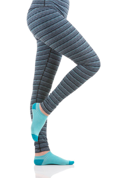Close up view of woman legs in colourful striped thermal pants and blue socks from the side view standing on one leg with other led raised - Photo, Image
