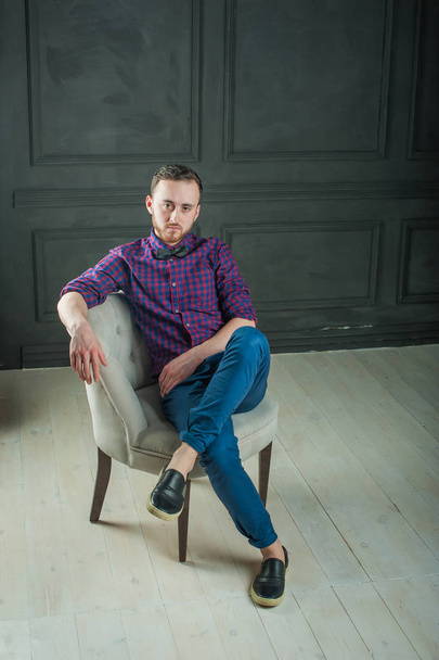 studio portrait of a young hipster man on a dark wall background in a blue shirt and jeans.  - Фото, изображение