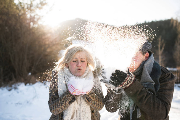 Casal sênior bonito soprando neve na natureza ensolarada inverno
 - Foto, Imagem