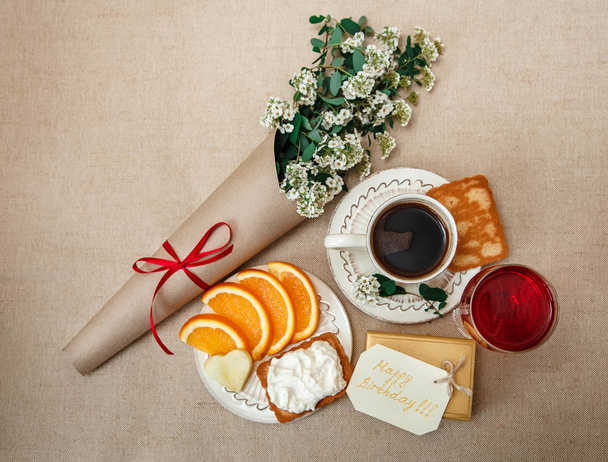 romantischer Geburtstag gesundes Frühstück.Tasse Kaffee, geschnittene Orange, Keks mit Hüttenkäse.Glas rotes Getränke.Wunschkarte mit Blumen.Geschenk in goldener Schachtel - Foto, Bild