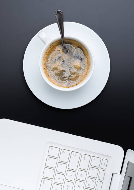 Белая чашка кофе на тёмном фоне с ноутбуком. Вид сверху
. - Фото, изображение