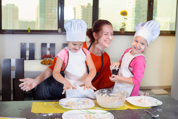 Two lovely children together with mother preparing a cake - Foto, afbeelding