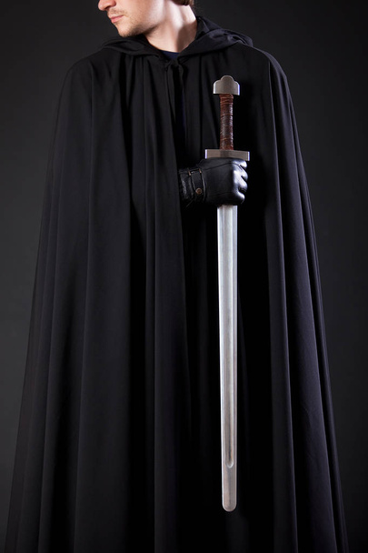 Portrait of a courageous warrior wanderer in a black cloak and sword in hand. - Φωτογραφία, εικόνα