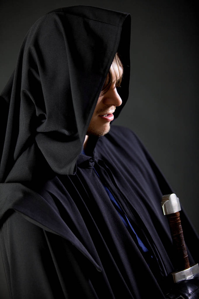 Portrait of a courageous warrior wanderer in a black cloak and sword in hand. - Fotografie, Obrázek