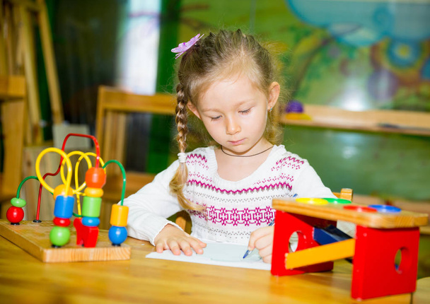Αξιολάτρευτο παιδί κορίτσι σχέδιο με χρωματιστά μολύβια στο παιδικό δωμάτιο. Παιδί στο νηπιαγωγείο στην προσχολική τάξη Μοντεσσόρι. - Φωτογραφία, εικόνα