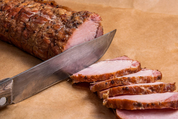 Sliced smoked meat or ham and knife on brown packing paper. - Photo, Image