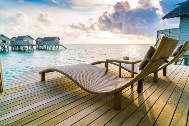 Two deck chairs on the wooden floor in water villa sunset time , - Photo, Image