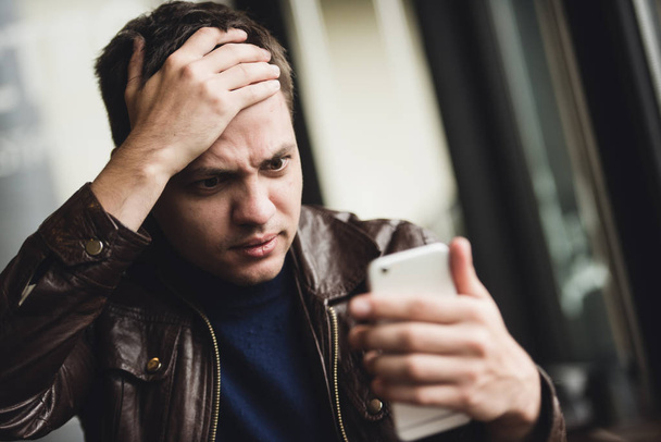 Huonoja uutisia. Masentunut nuori mies ilmaisee negatiivisuutta lukiessaan viestiä matkapuhelimella
 - Valokuva, kuva