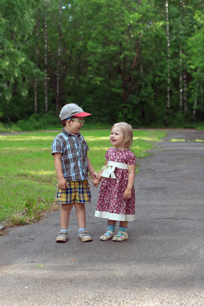 Malá hezká dívka a chlapec se smát a držet se za ruce v parku v sunny - Fotografie, Obrázek