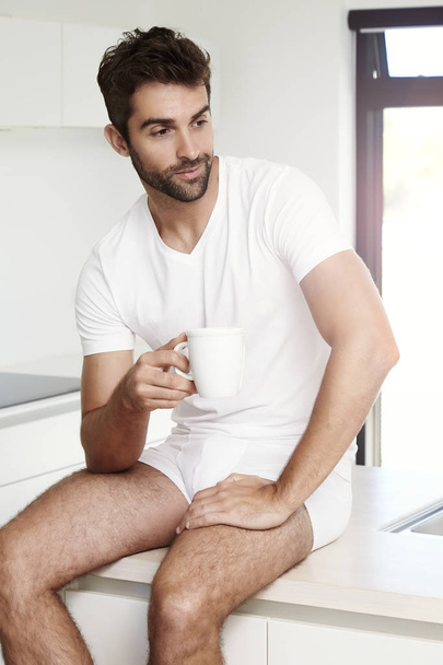 Man in underwear sitting with coffee cup - 写真・画像